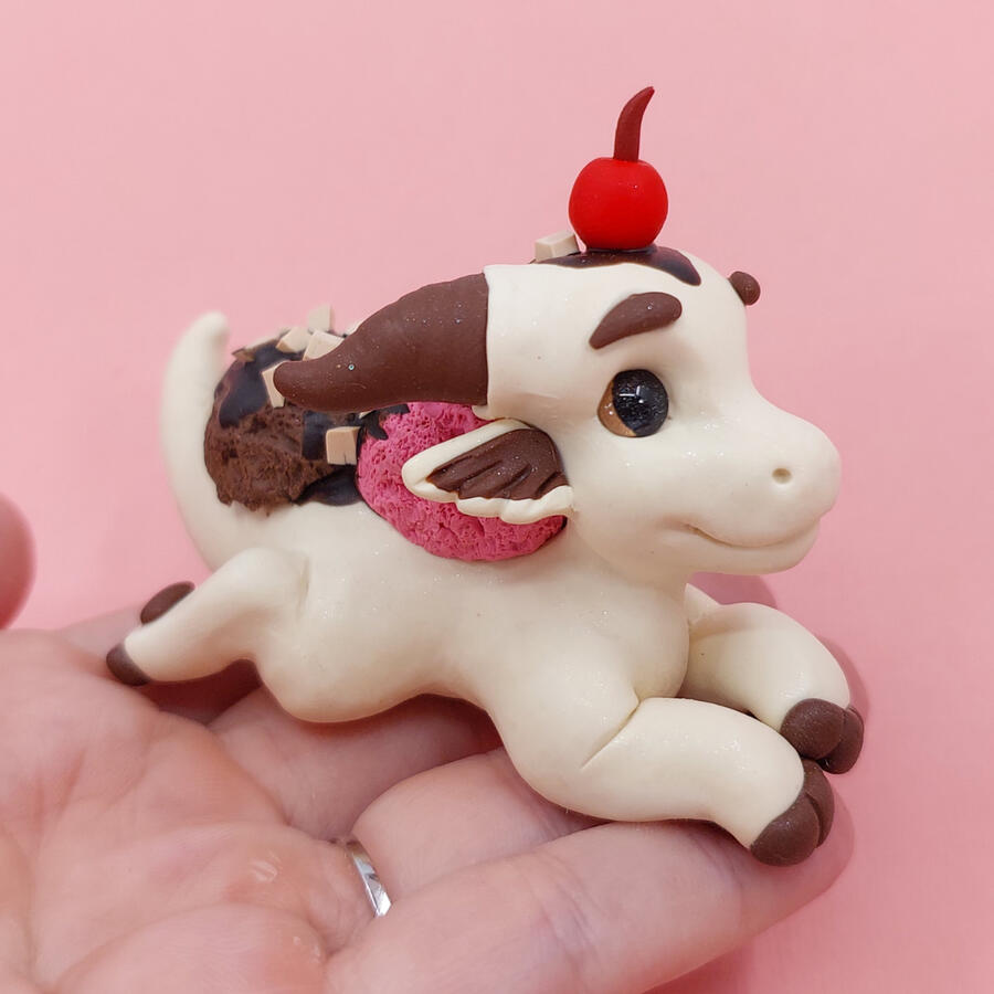 Pale yellow clay dragon lying outstretched on an upturned palm. It has a sculpted cherry on its head, and ice-cream on its back. Pale yellow clay dragon lying outstretched on an upturned palm. It has a sculpted cherry on its head, and ice-cream on its back.