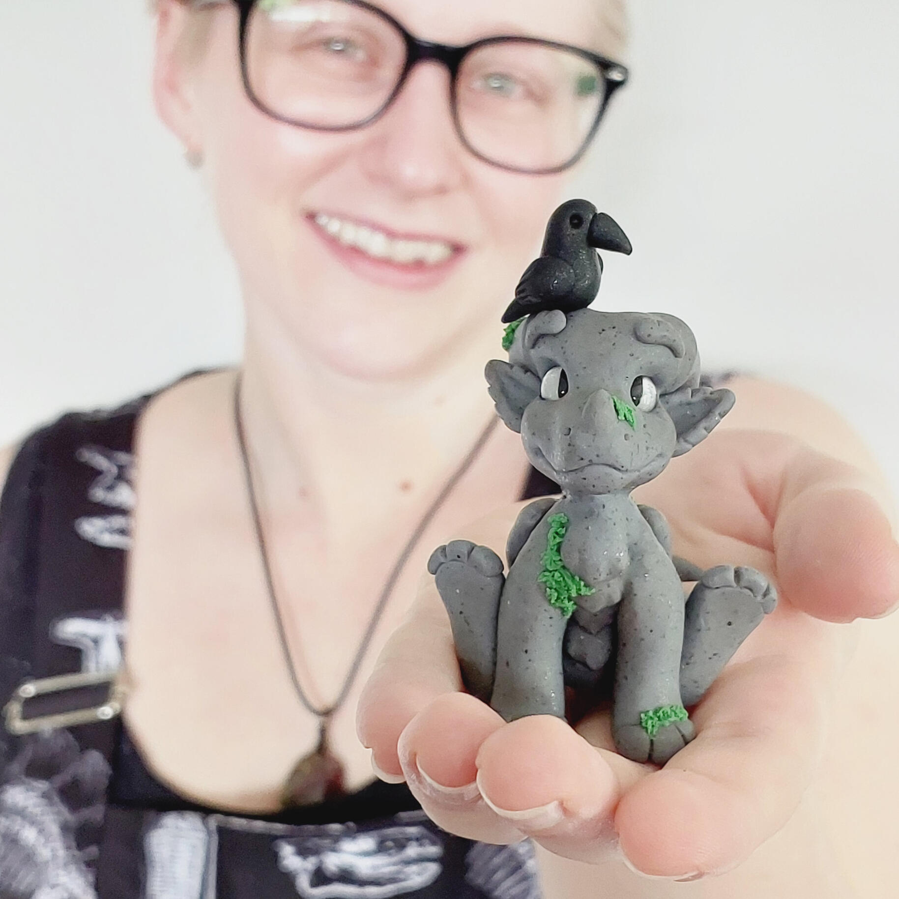 A grey clay dragon sitting on the upturned hand of a caucasian female facing the camera.